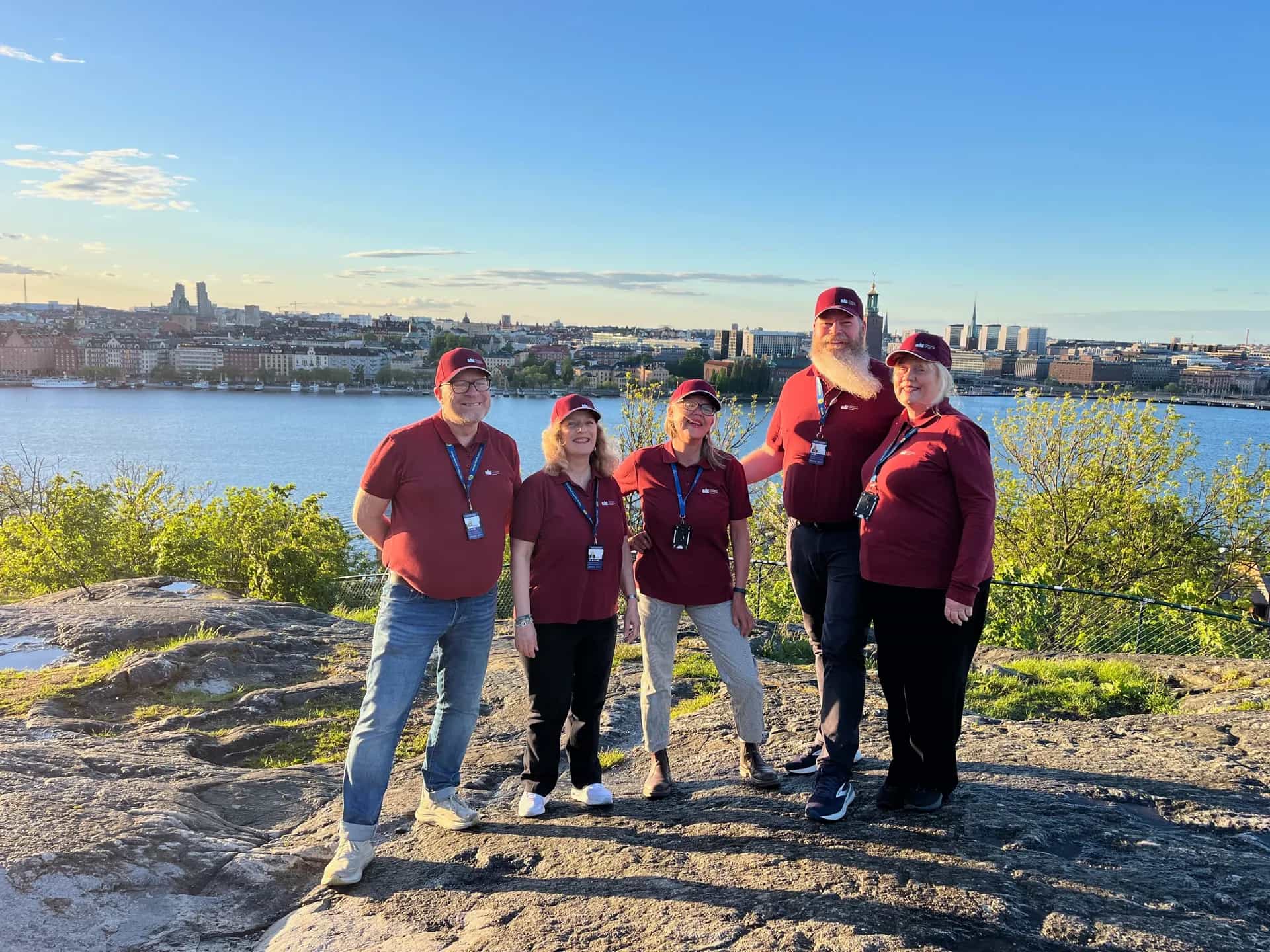 Five Stockholm guides in matching clothes stand on a cliff overlooking Stockholm's city and water